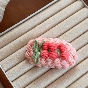 Détail de la pince à cheveux crochetée avec base rose et motifs de baies rouges en 3D