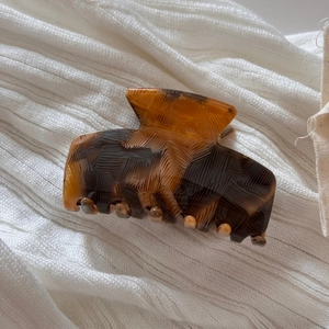 Close-up of tortoise shell acetate hair claw clip with rippled texture on white fabric