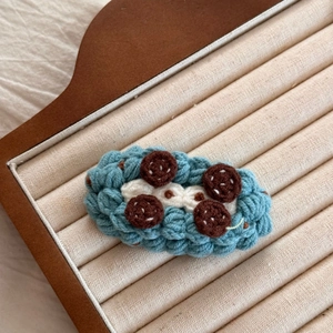 Détail d'une pince à cheveux au crochet bleue avec textures blanches et motif de biscuit