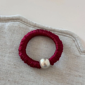 Close-up of wine red pleated silk hair tie featuring a large shiny silver metallic bead