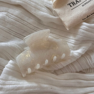 Detail shot of marble textured acetate hair claw clip on white fabric background