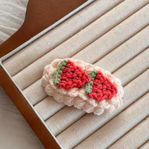 Détail d'une barrette à fraise crochetée main avec base en tricot rose et feuilles vertes