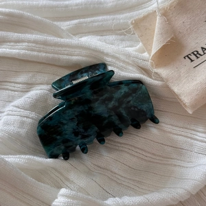 Detail of marble pattern acetate hair claw clip in dark green on white knit fabric