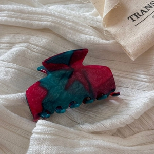 Detail of medium acetate hair claw with red and green marble texture on knit fabric