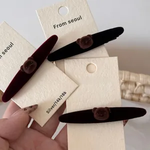 Detalle de pinzas para el cabello en terciopelo con oso sobre cartón beige rugoso