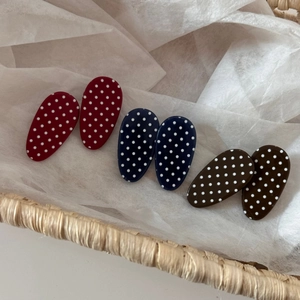 Close-up of oval polka dot hair clips in red, navy, and brown within a woven basket
