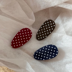 Three oval polka dot hair clips in red, brown, and navy blue on white textured paper