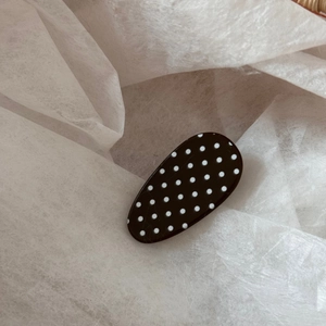 Close-up of a glossy black oval hair clip with white polka dots on soft tissue paper