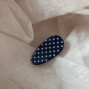 Close-up of a glossy navy blue hair clip with white polka dots on textured paper