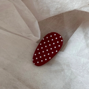 Detailed view of an oval red hair clip with white polka dots on a soft white paper background