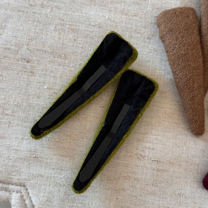 Detailed macro view of green wool fabric hair clips on a textured beige fabric background