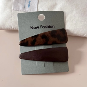 Detail view of two pointed leopard print and brown leather hair clips on display card