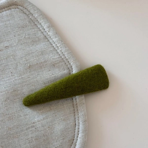 Detail of an olive green knit wool hair clip on a minimalist beige linen surface