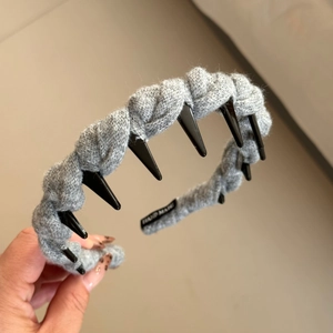 Détail d'un serre-tête tressé gris montrant les dents antidérapantes et l'étiquette fait main