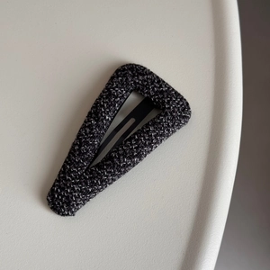 Detail of grey tweed fabric texture on a triangle hair claw clip with metallic base