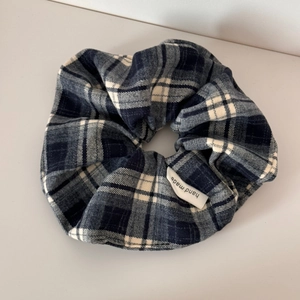 Detail of blue and grey plaid fabric scrunchie featuring a white hand made woven label