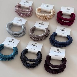 Detail of nine multi-color satin scrunchies displayed on branded white cards