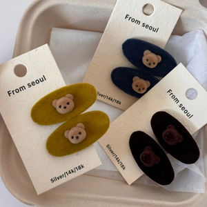 Detailed view of six velvet bear hair clips in yellow, blue, and black on a gift card