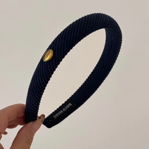 Detailed macro view of navy blue ribbed fabric headband with oval gold Korea metal tag