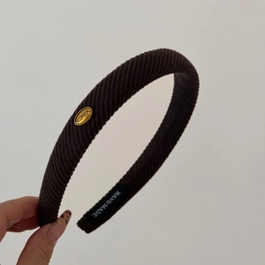 Detail view of brown textured knit headband with oval gold logo and handmade label