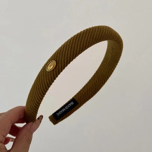 Macro detail of mustard yellow knit headband with golden oval metal label and handmade tag