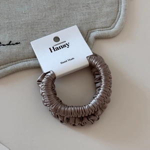 Detailed view of coffee satin scrunchie showing glossy texture and Hansy handmade tag