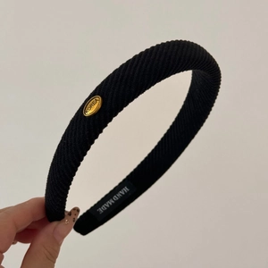 Close-up of black ribbed headband featuring an oval gold Korea tag and handmade label