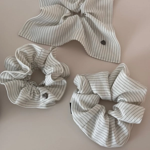 Detail of three white striped hair scrunchies with heart charms on ivory background