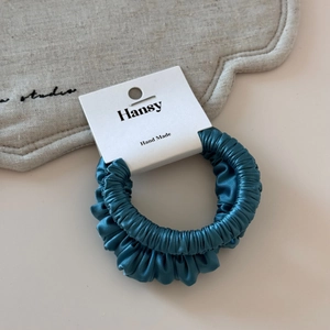 Detailed macro view of dark cyan satin scrunchie with silky texture and handmade tag