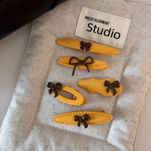 Close-up of 5-piece yellow hair clip set with brown bows on grey linen background