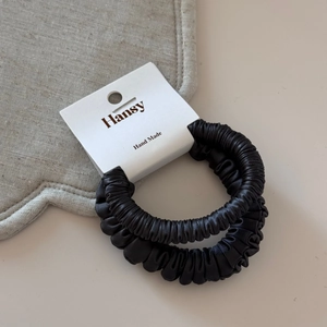 Macro detail of two black satin scrunchies with glossy texture on luxury card packaging