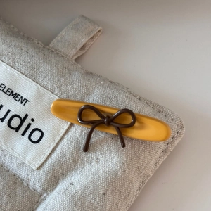 Detailed close-up of a bright yellow hair clip with a dark brown ribbon bow on quilted fabric