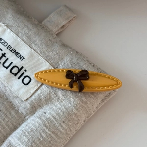 Detail of yellow oval hair clip with brown bow and premium stitching on linen background