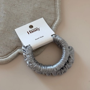 Detail of silver grey satin scrunchie with Hansy branded display card on beige mat