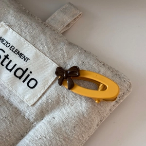 Close-up of matte yellow oval hair clip with dark brown 3D bow accent on beige canvas