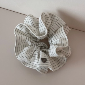 Detail of white striped scrunchie featuring a vintage grey heart-shaped metal charm
