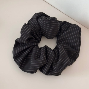 Close-up of black oversized scrunchie with white stripes and smooth fabric texture