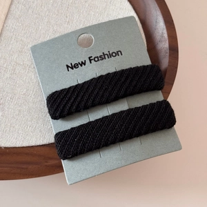 Detail view of two black twill fabric rectangle hair clips on a New Fashion display card