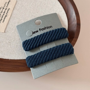 Detailed view of two dark blue twill knit hair scrunchies on a minimalist display card
