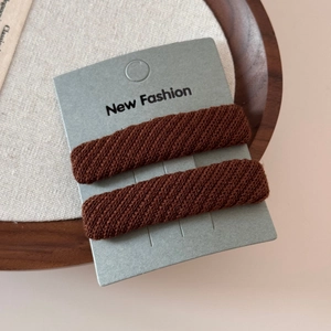Detail view of dark brown twill fabric BB hair clips on a New Fashion card display