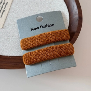 Detail of two orange-brown knit fabric sponge hair clips on a grey display card