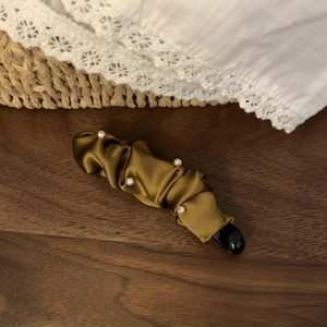 Detailed macro of golden pleated satin banana clip with elegant pearls on dark wood