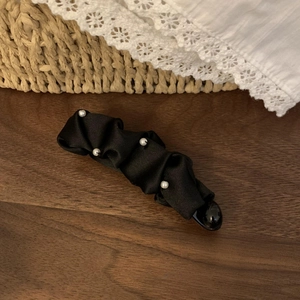Detail of black pleated fabric banana clip featuring white pearl embroidery on wood