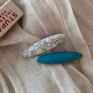 Detail showing marble texture acetate hair clips with gold metal base on beige fabric