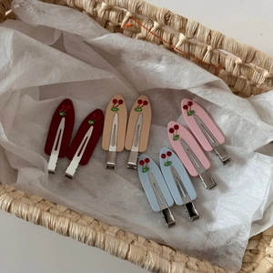 Detailed view of eight acetate cherry hair clips in four colors on white tissue paper