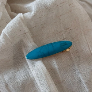Close-up of blue marble pattern acetate hair clip with gold metal base on beige fabric