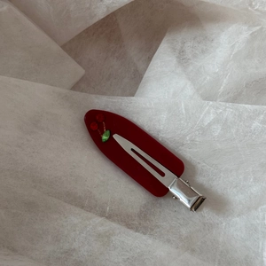 Close-up of red cherry hair clip with sparkling rhinestones on textured white background