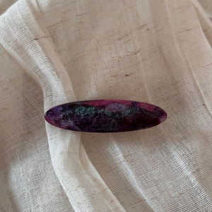 Close-up of vintage oval acetate hair clip with purple marble pattern on beige fabric