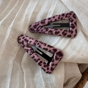 Dettaglio di fermagli per capelli leopardati rosa con texture vellutata su tessuto beige