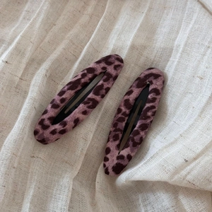 Dettaglio di due fermagli per capelli viola leopardati su sfondo di tessuto testurizzato